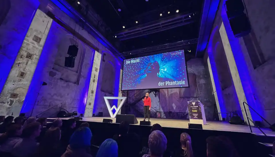 Dorothee Töreki: Keynote auf der großen Bühne Dorothee Töreki hält eine Keynote-Präsentation auf einer großen Bühne mit blauer Beleuchtung und dem Bildschirmtitel "Die Macht der Phantasie" vor Publikum.