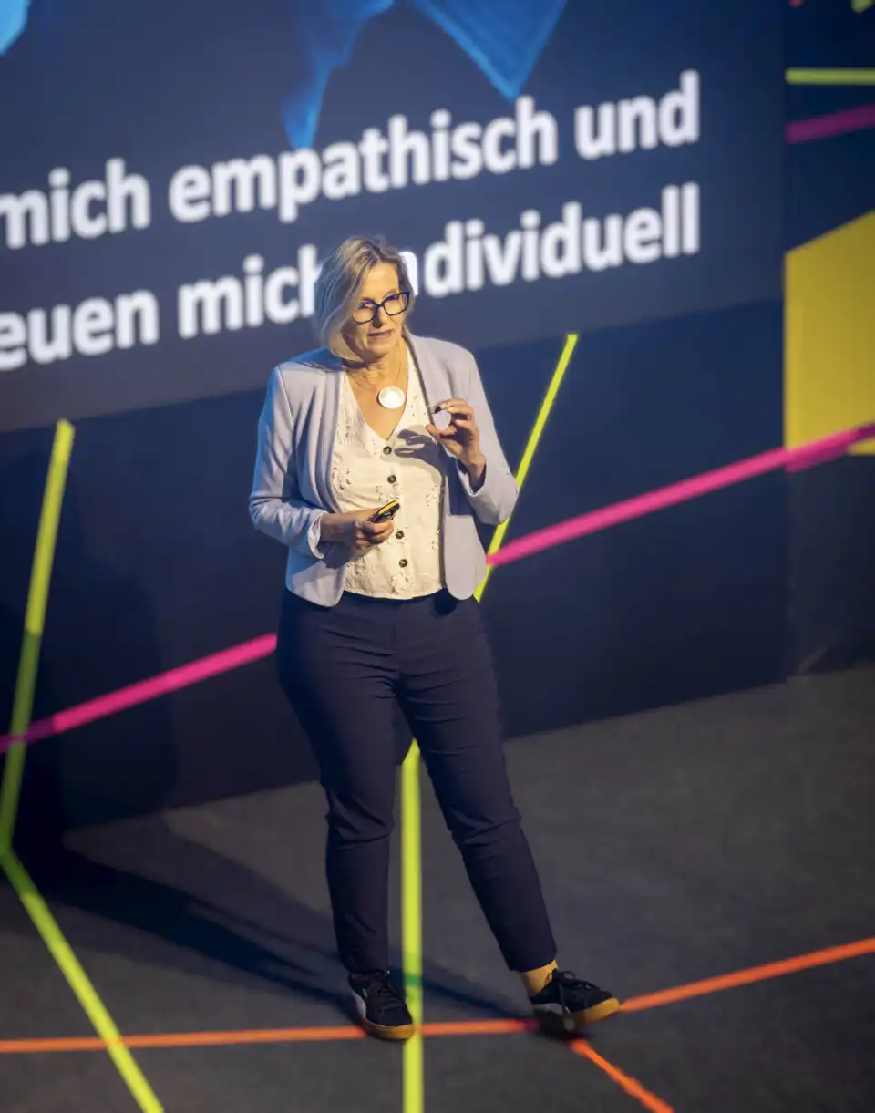 Dorothee Töreki: Vorträge über KI & Digitalisierung Dorothee Töreki gestikulierend bei Vortrag vor Leinwand mit Text.