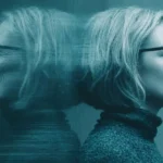 Profil einer Frau mit Brille, angelehnt an eine spiegelnde Wand in Blautönen.